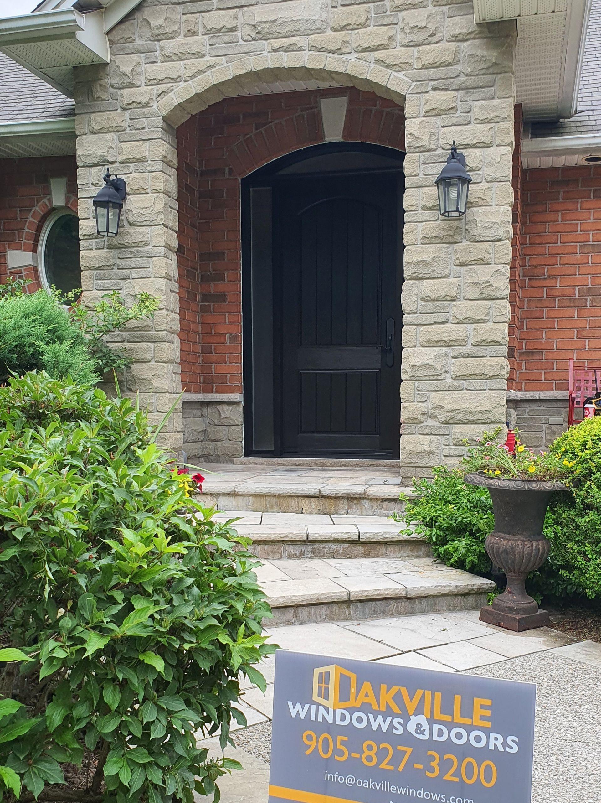 A sign for oakville windows and doors is in front of a brick house.