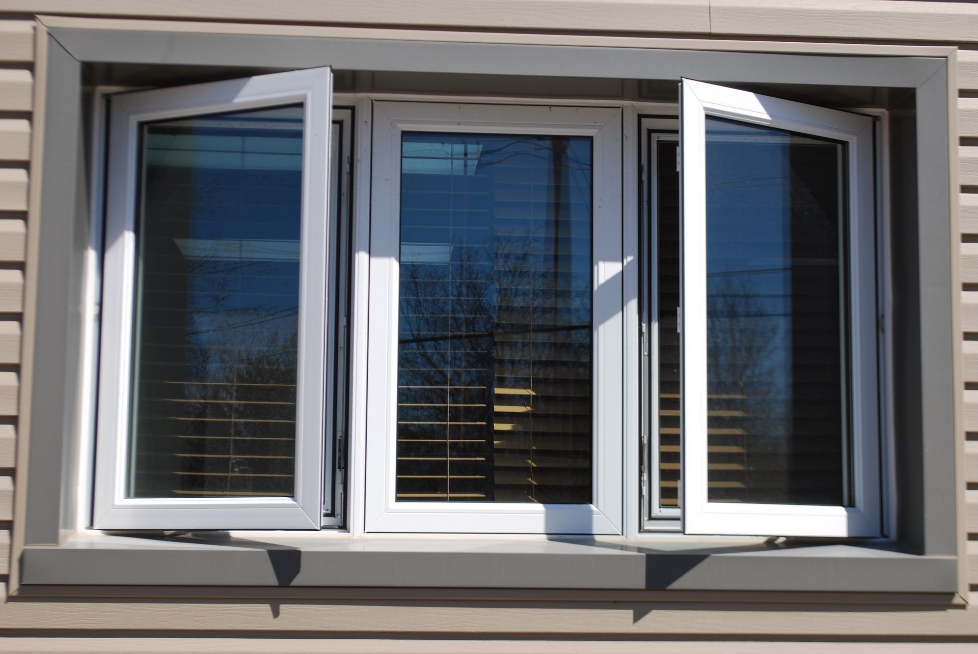 A row of white windows on a gray wall with one window open.