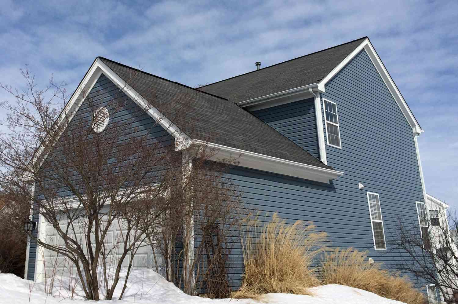 Blue house with a dark roof and snow on the ground.