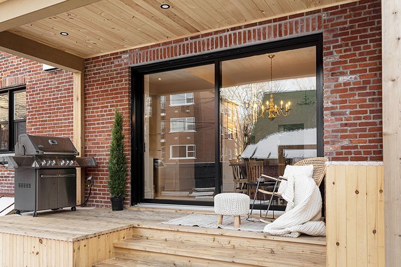 Outdoor patio with grill, sliding glass door, brick walls, wood deck, and a glimpse of the interior.