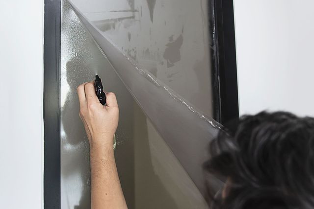 A person sprays a mist of water onto a windowpane while installing or cleaning a sheet of adhesive film.