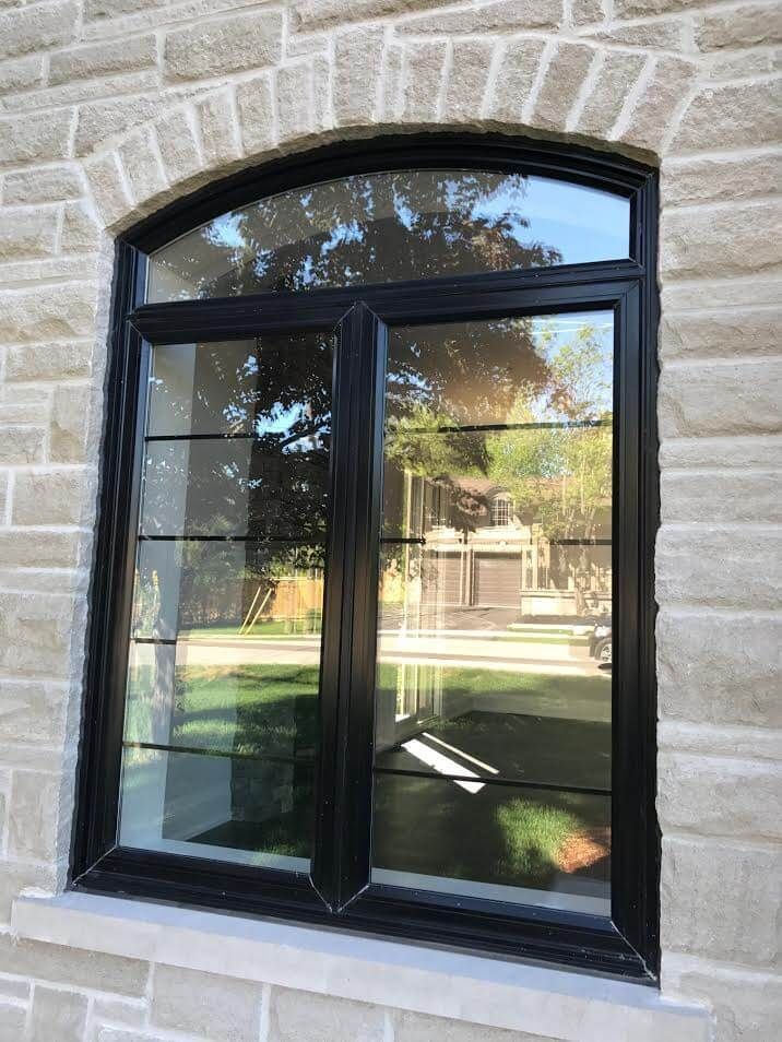 A window with a black frame is on a brick wall.