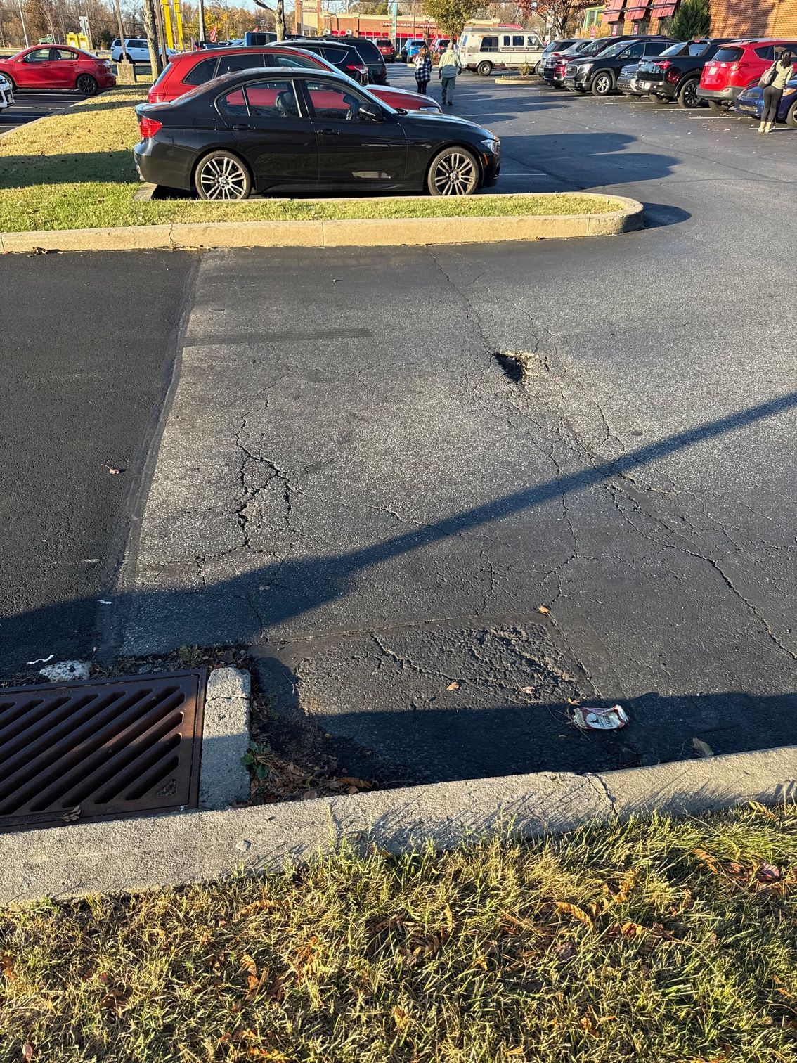 A Black Car Is Parked in A Parking Lot Next to A Drain.