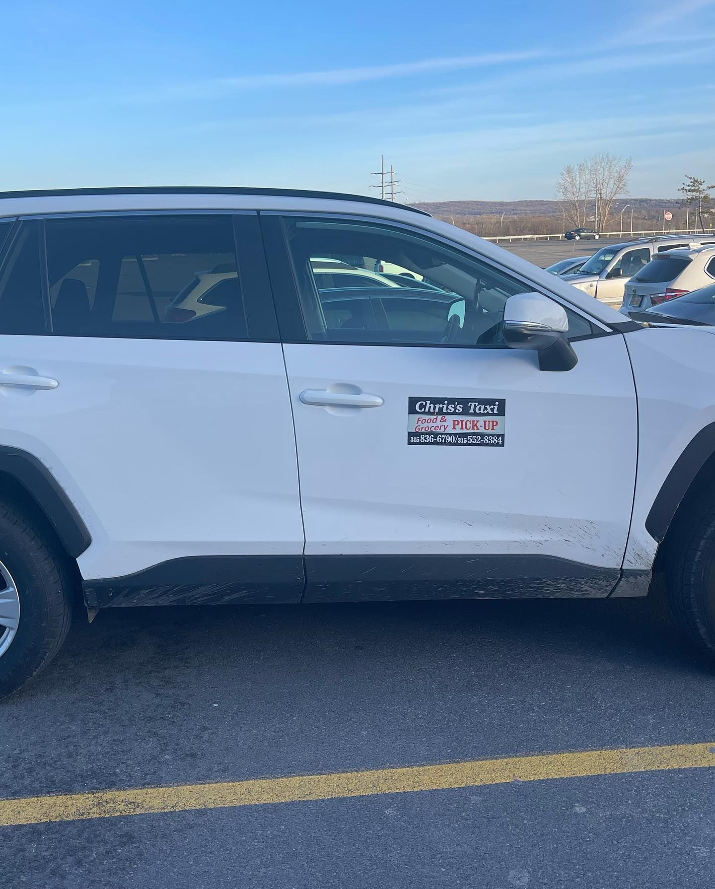 A white SUV parked in a lot, featuring a rectangular business logo sticker on the front passenger door.