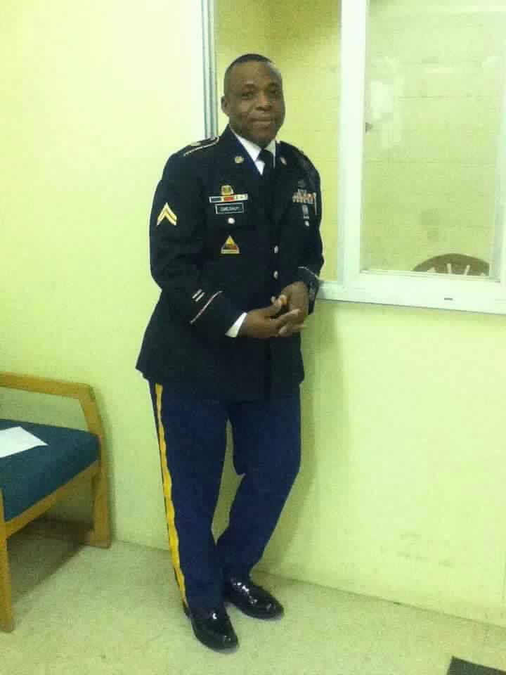 A person in an Army Service Uniform standing indoors near a light-colored wall and a window.