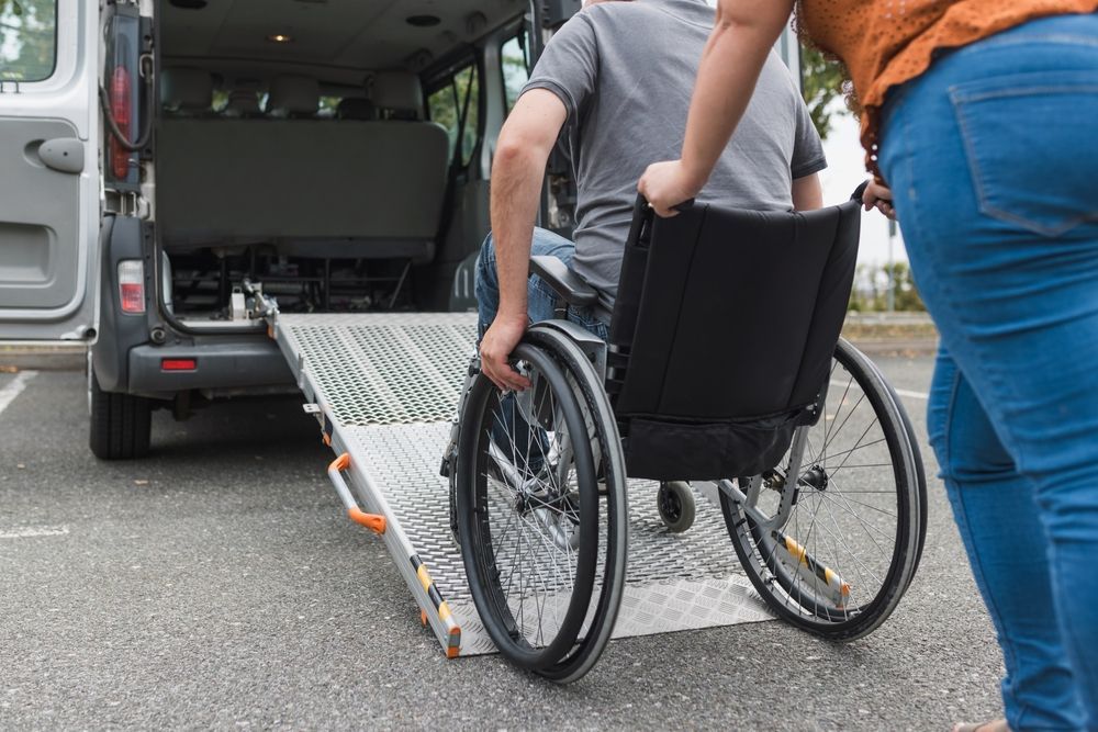 A person pushes a manual wheelchair up a portable ramp into the back of a van.