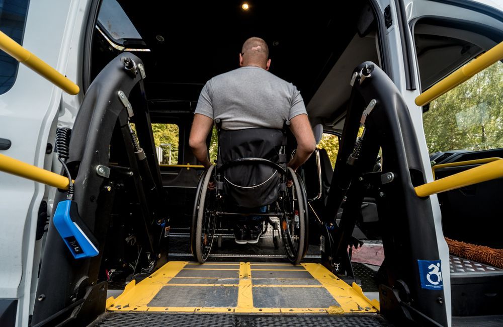 A person in a wheelchair positioned on a yellow-bordered ramp at the back of a van, prepared to enter.