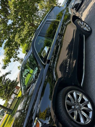 A side-angle view of a shiny black SUV parked on asphalt outdoors, with trees and a building in the background.
