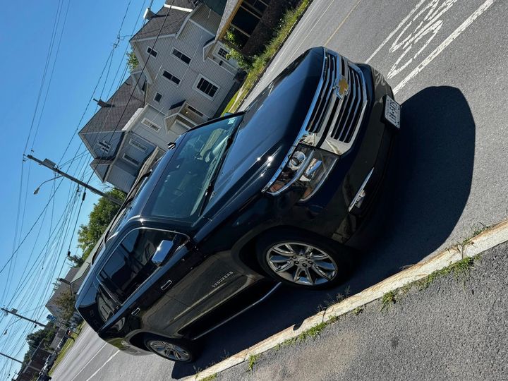A dark-colored Chevrolet SUV parked on an asphalt street with a multi-story building in the background.