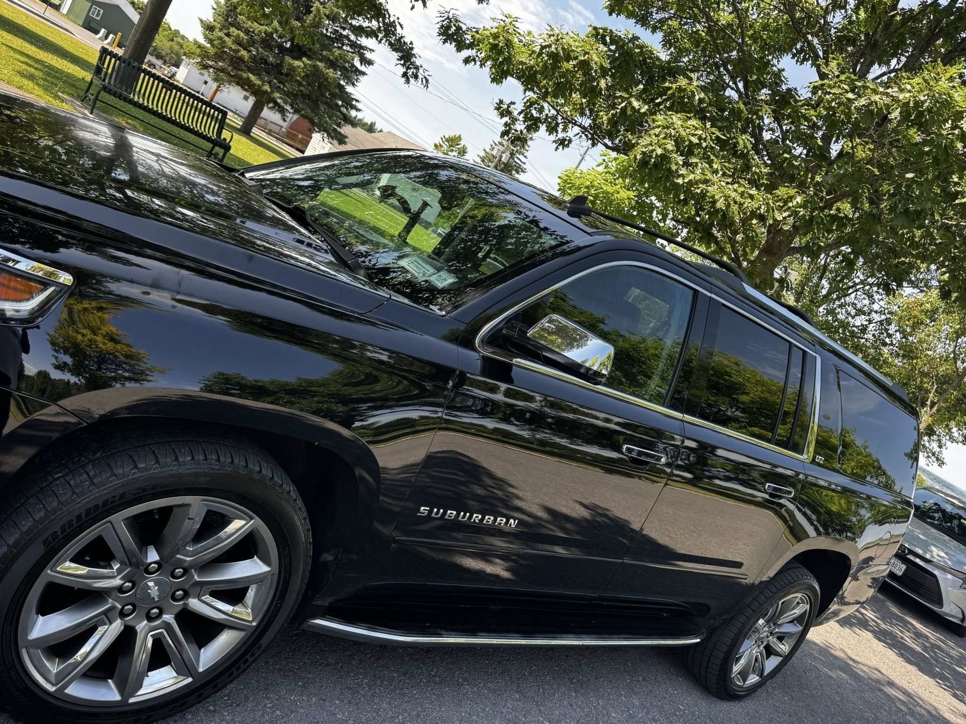 A black Chevrolet Suburban SUV parked on an asphalt lot near trees.