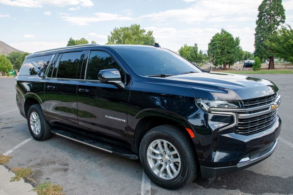 A black Chevrolet Suburban SUV parked in an outdoor parking lot under a blue sky.