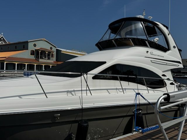 A white motor yacht moored at a marina dock near a multi-story building under a clear blue sky.