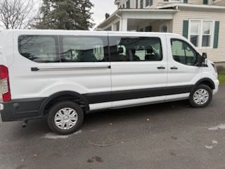 A white Ford Transit passenger van parked on a paved driveway in front of a house.