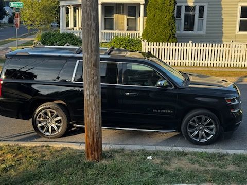 A black Chevrolet Suburban SUV parked on the side of a residential street, partially obscured by a utility pole.