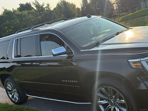 A black Chevrolet Suburban SUV parked on a paved road with trees in the background during a sunset.