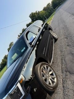A black SUV parked on the side of a paved road with trees in the background under a clear sky.