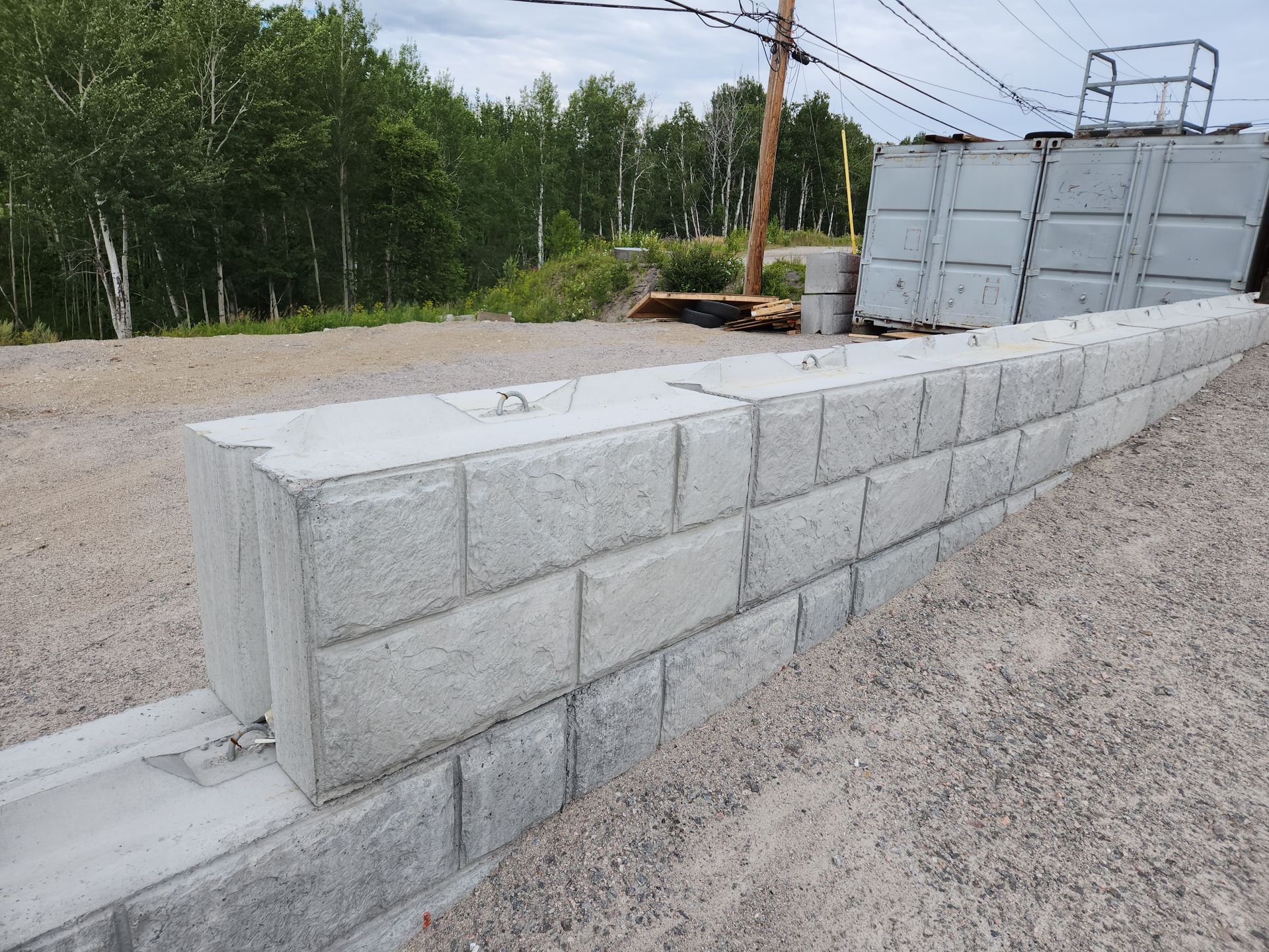 Un mur de béton est en cours de construction dans une zone de gravier avec des arbres en arrière-plan.