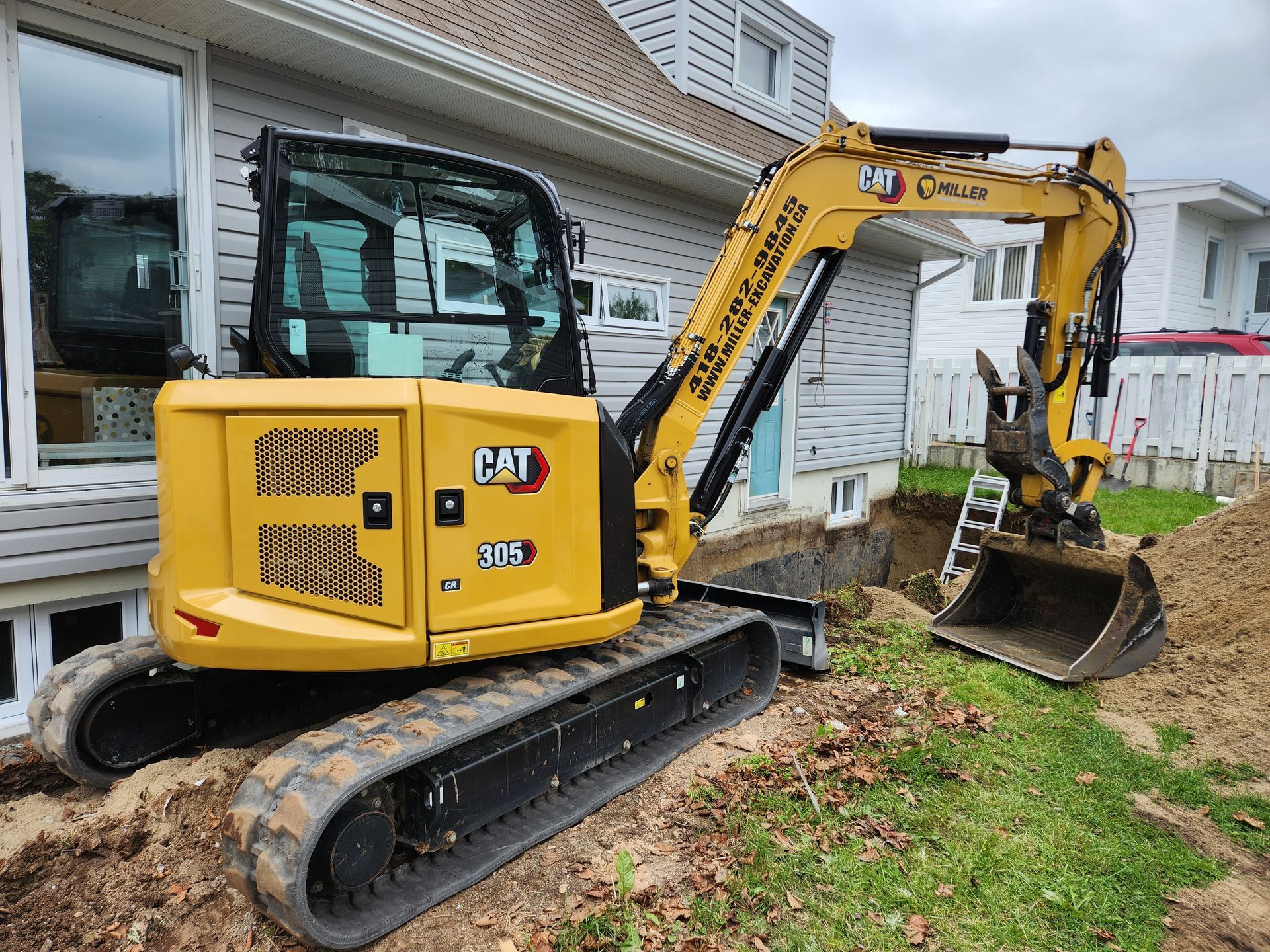 Mini-pelle Caterpillar jaune creusant près des fondations d'une maison.