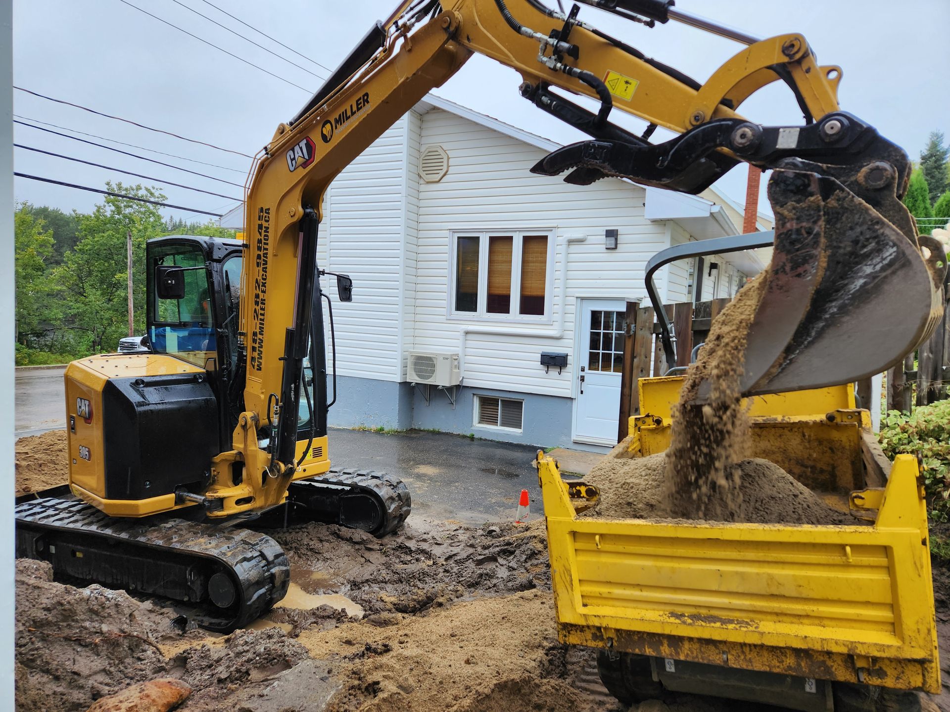 Une excavatrice jaune charge de la terre dans une benne à ordures.