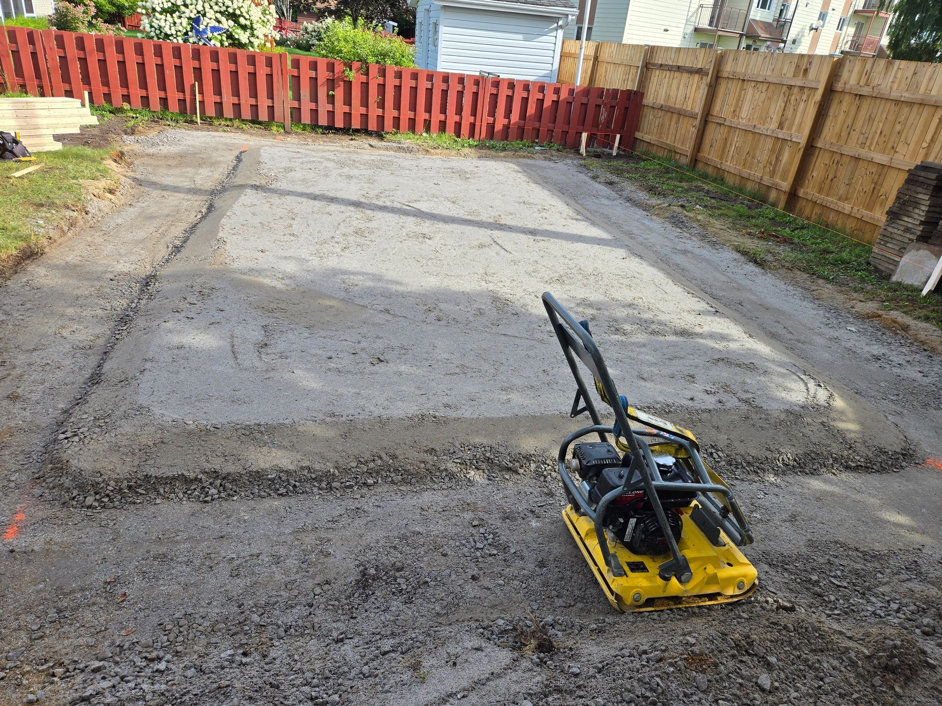 Une plaque vibrante jaune est posée sur une allée en béton.
