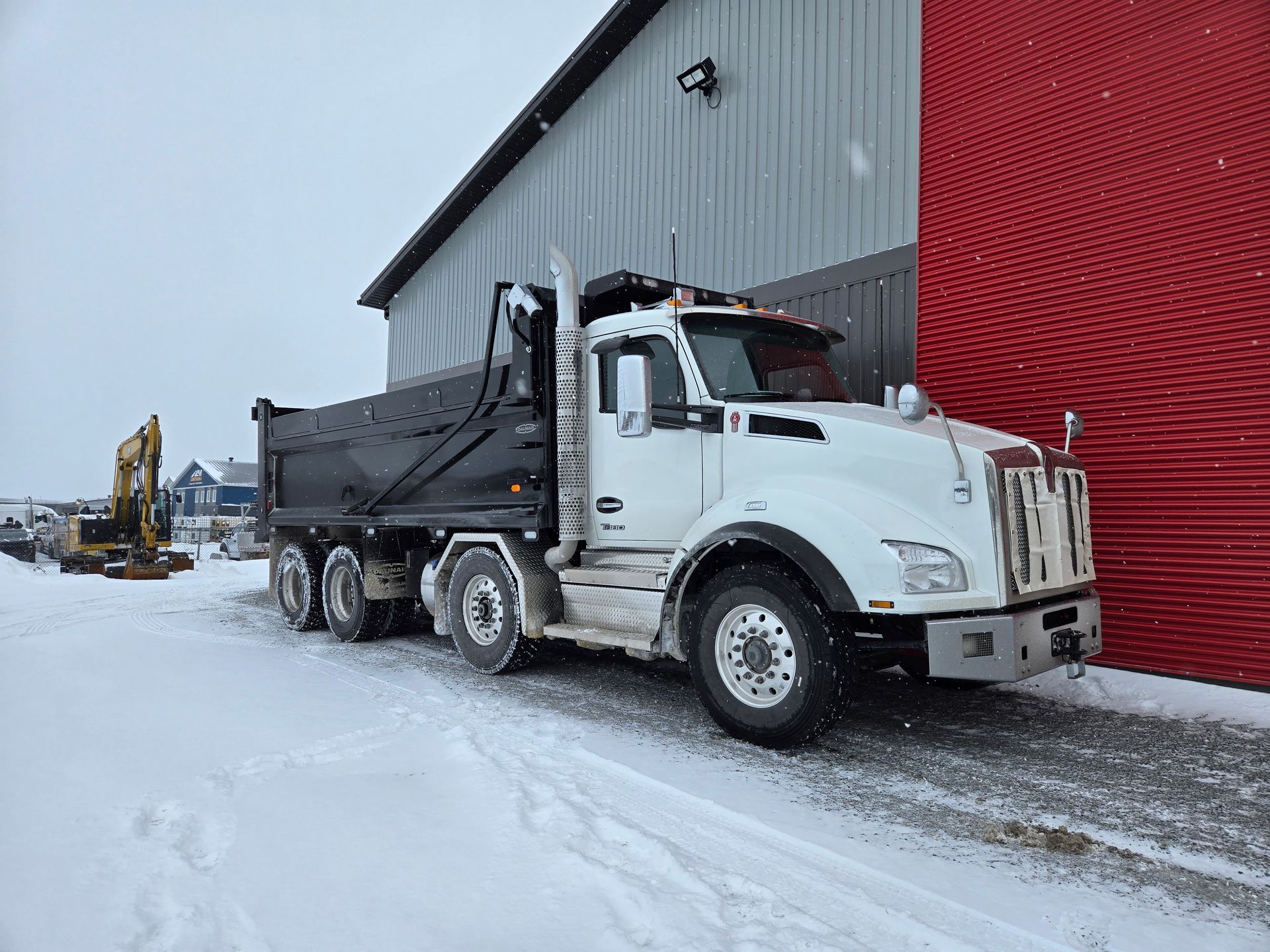 Un camion à benne basculante est garé dans la neige devant un bâtiment.
