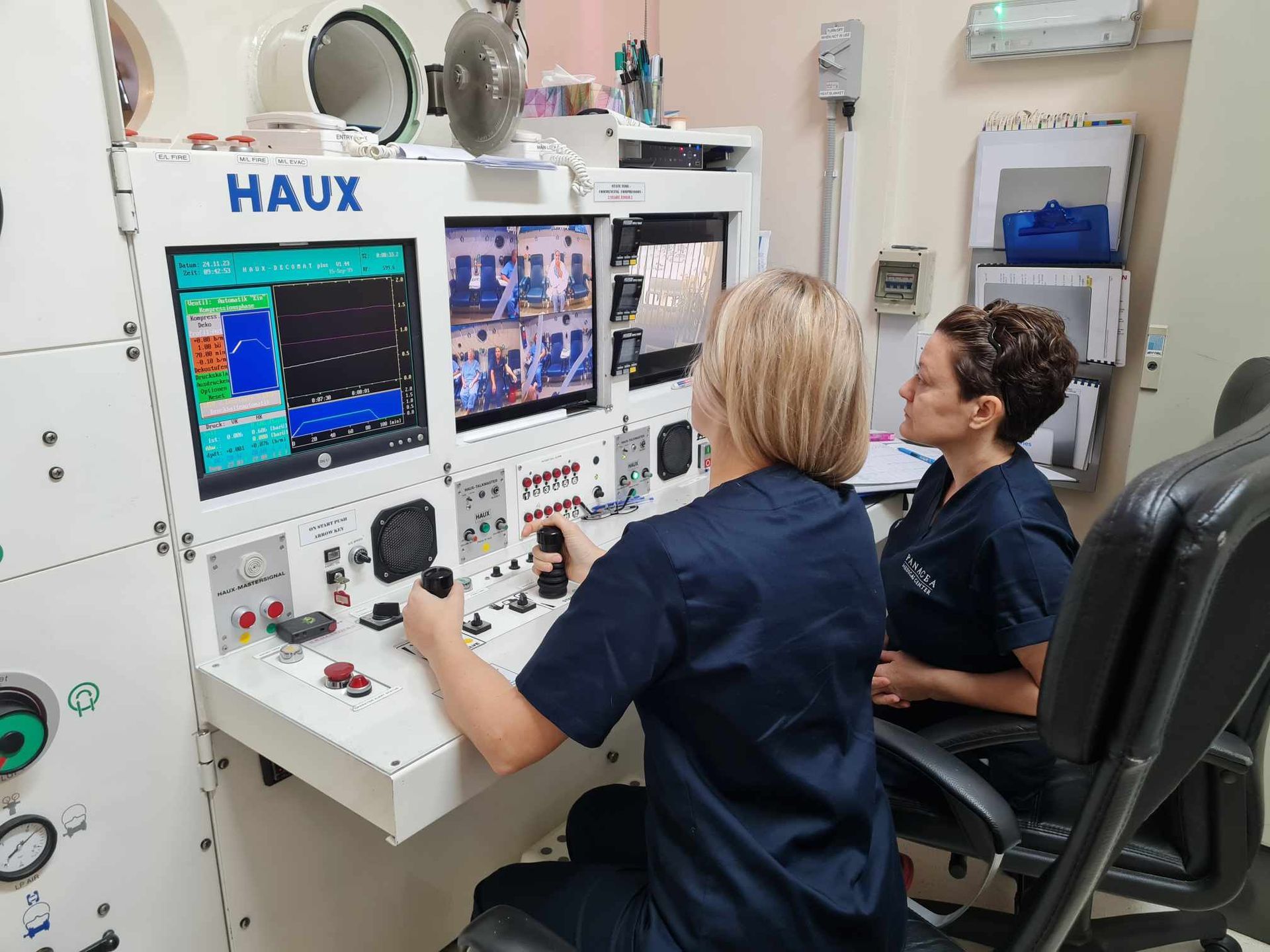 Two women are sitting in front of a haux control panel