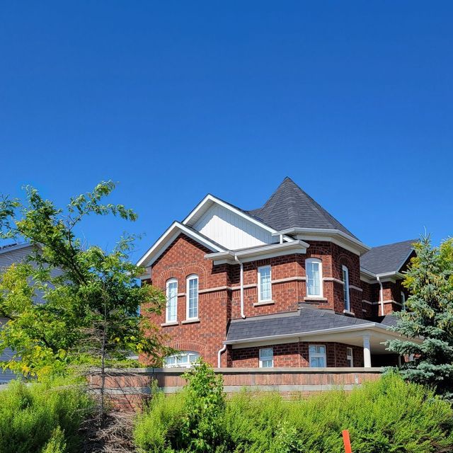 A large brick house is surrounded by trees and bushes