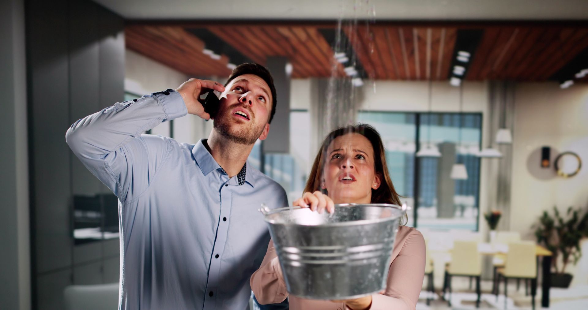 A man is talking on a cell phone while a woman holds a bucket.