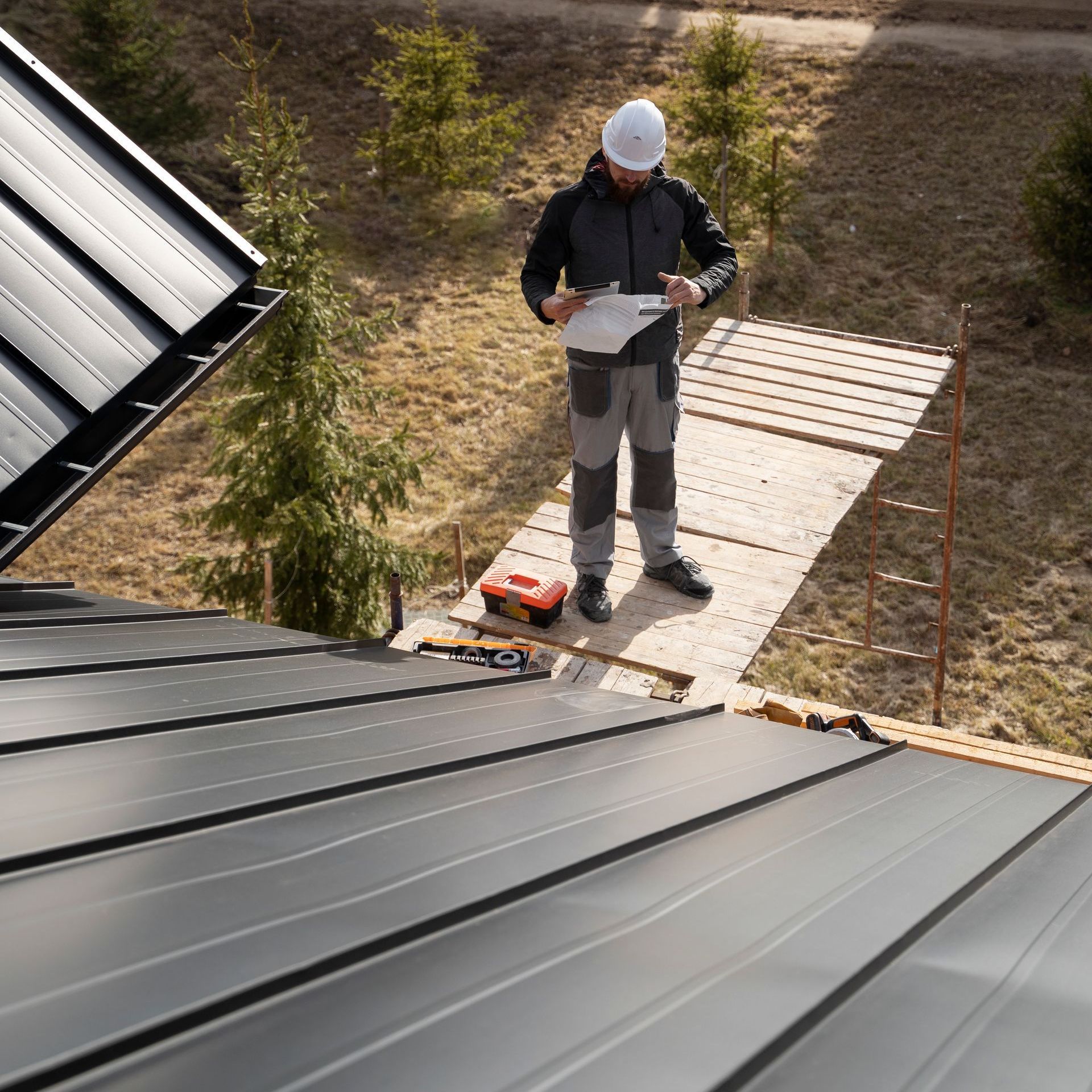 A man is standing on top of a roof looking at a clipboard.