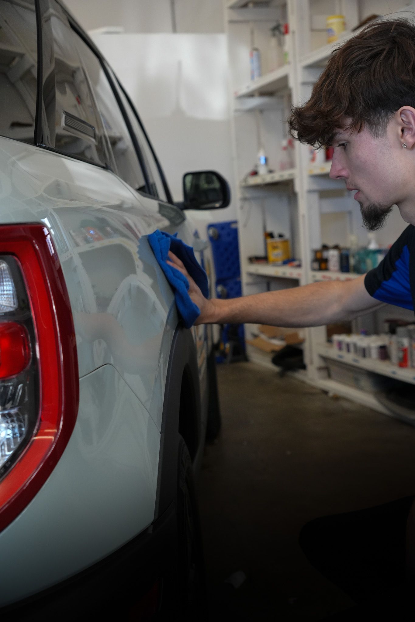 A man is cleaning a car with a sponge in a garage.