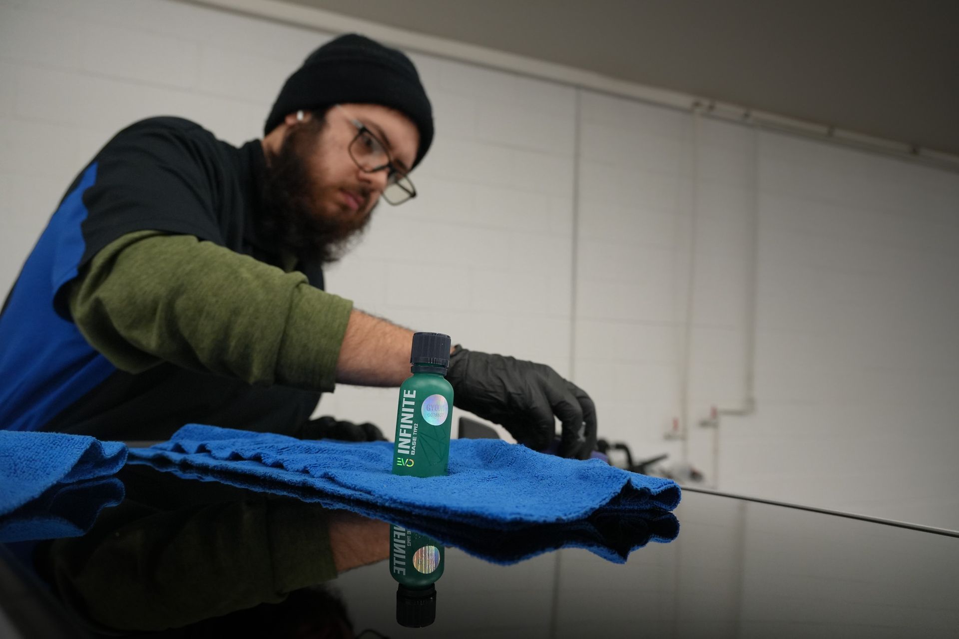 A man with a beard is cleaning a car with a towel.