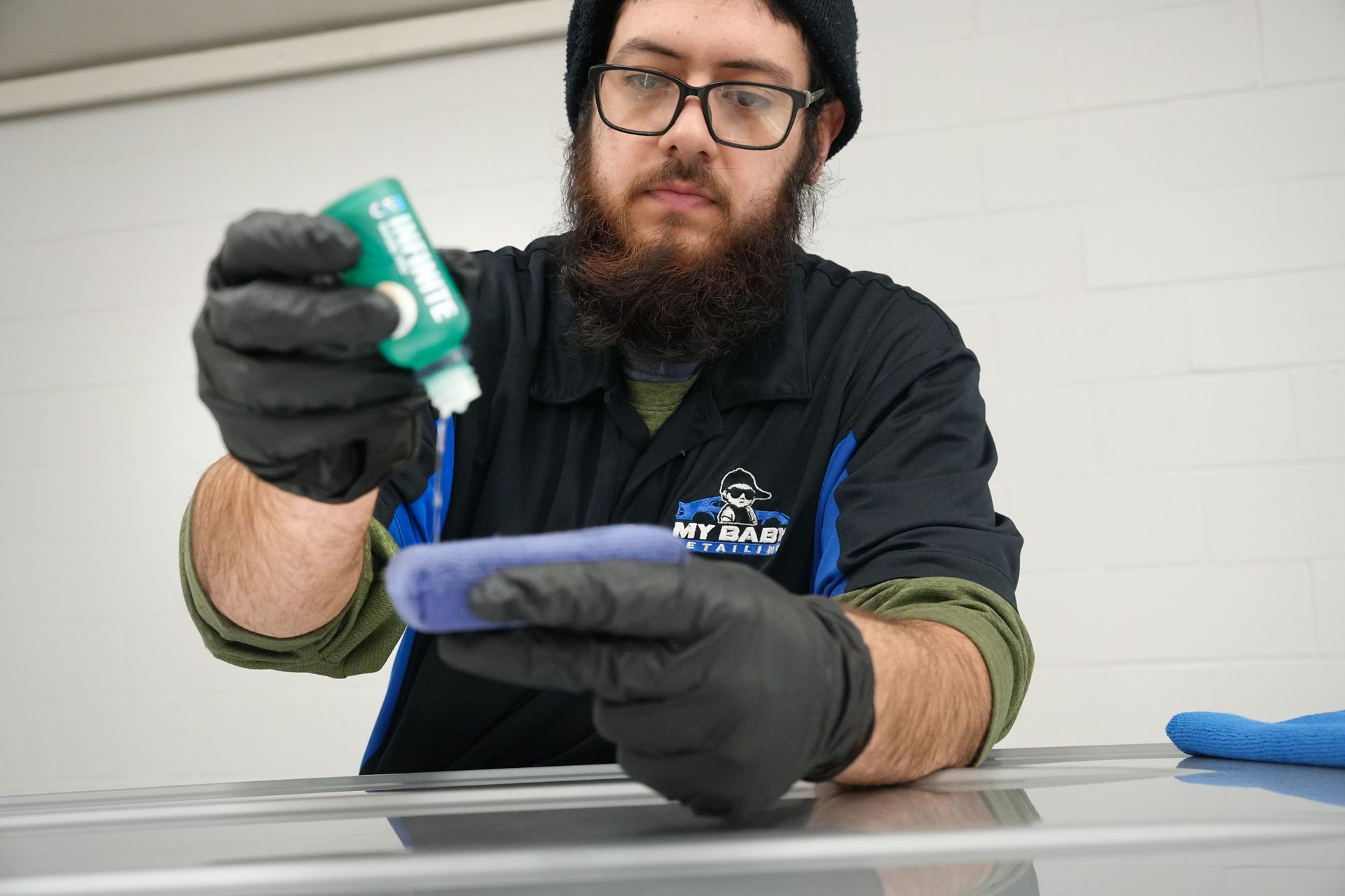 A man with a beard is applying a coating to a car.