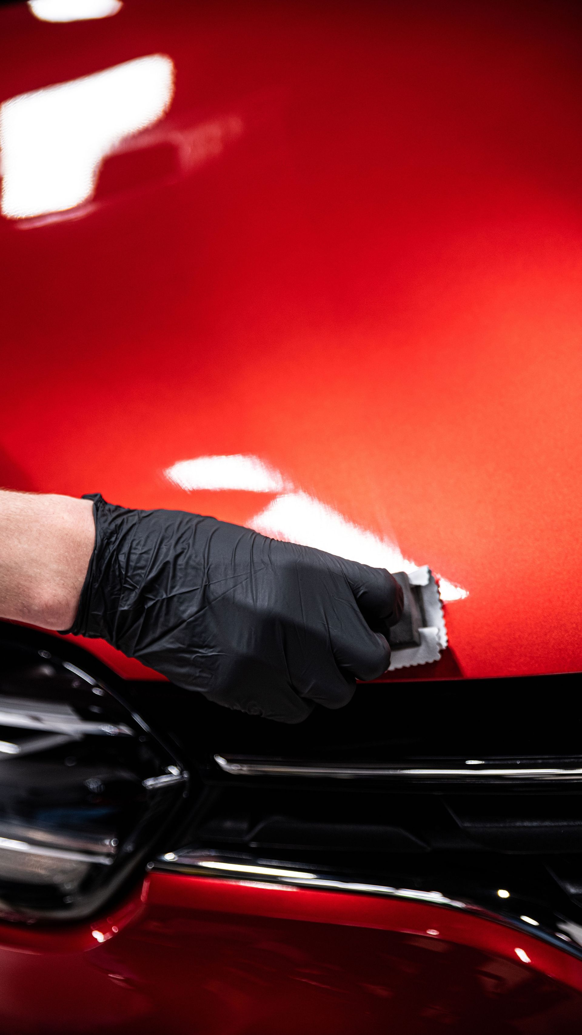 A person wearing black gloves is polishing the hood of a red car.