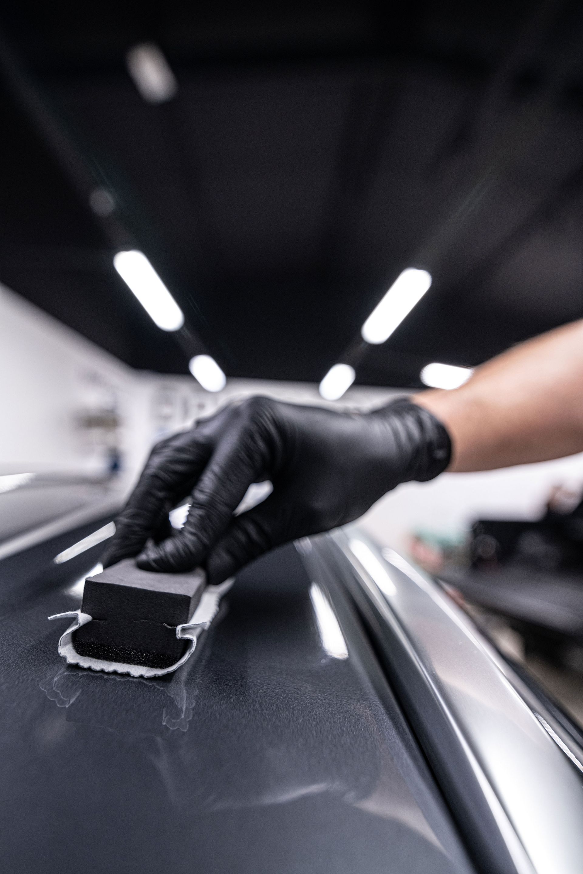 A person wearing black gloves is polishing the hood of a car.