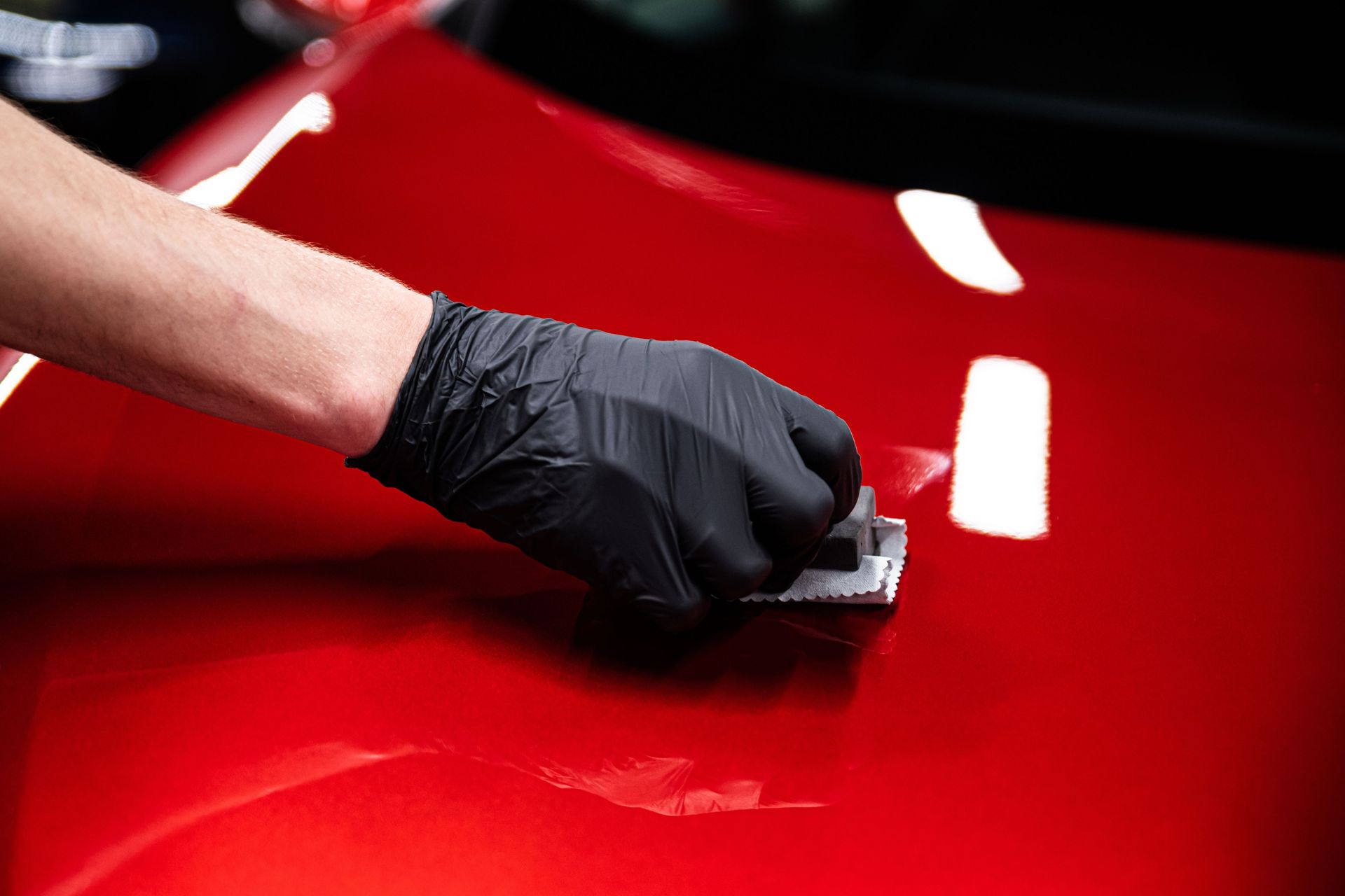 A person wearing black gloves is polishing a red car.