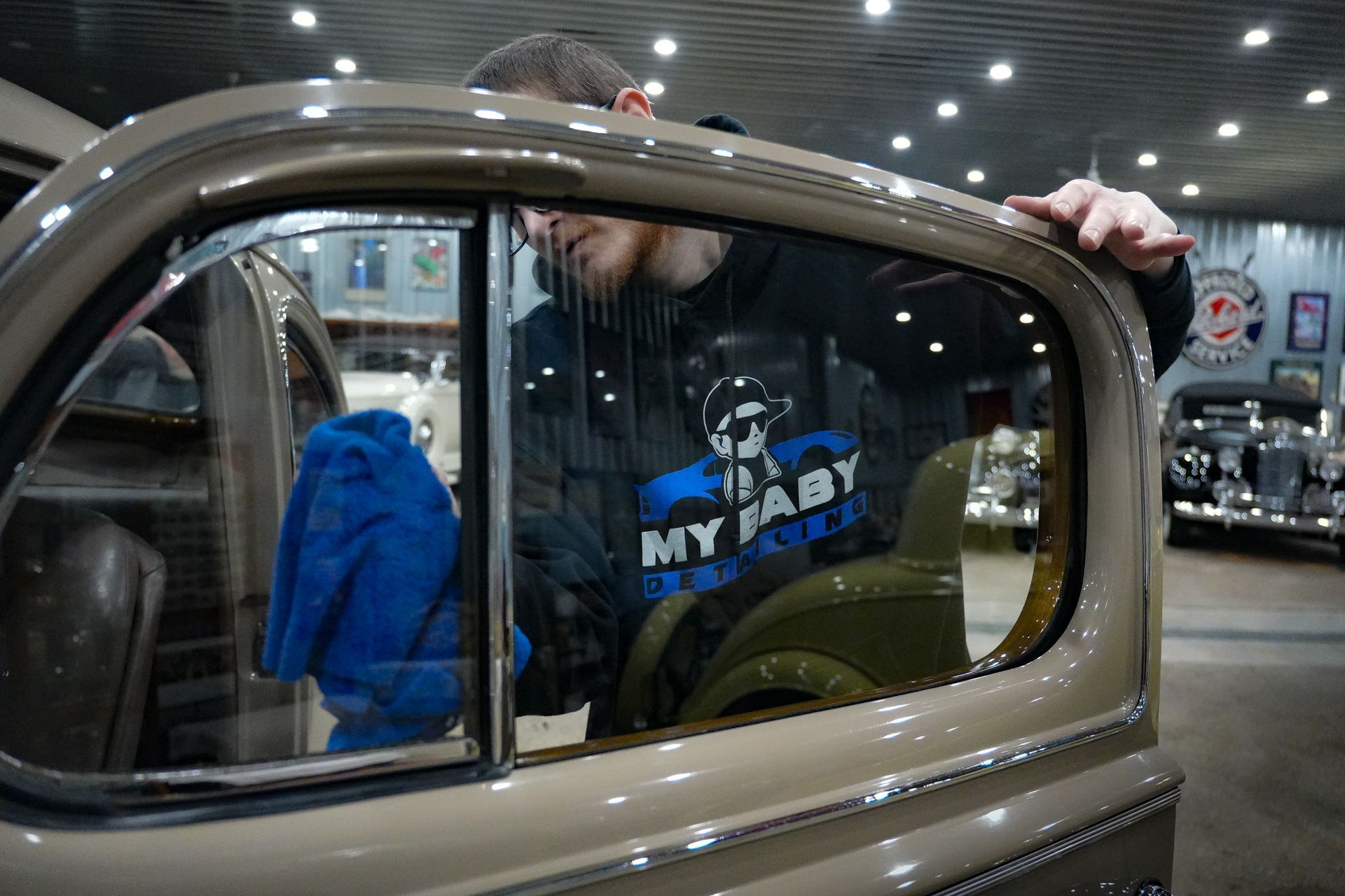 A man is cleaning the window of an old car.