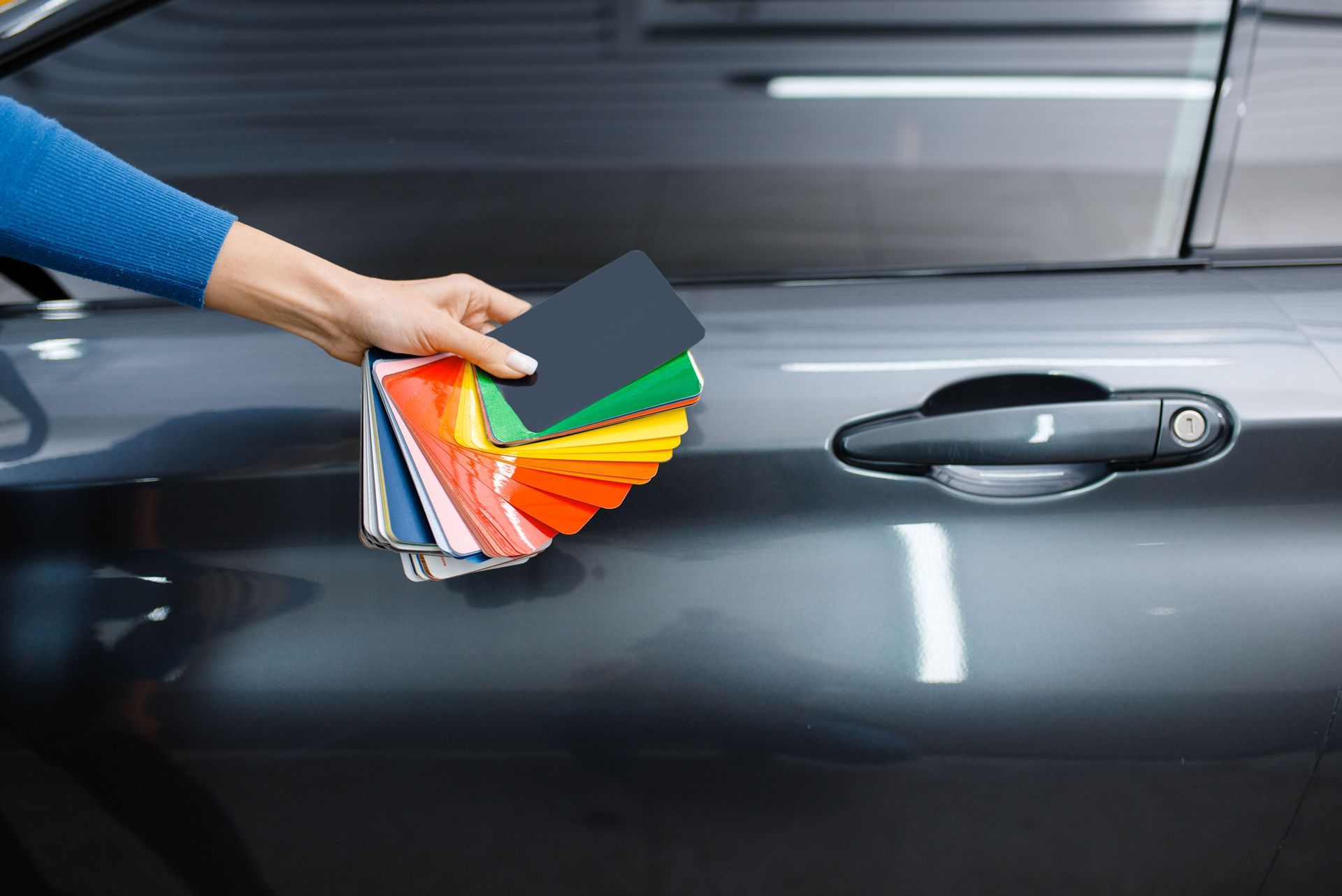 A person is holding a palette of colors in front of a car.