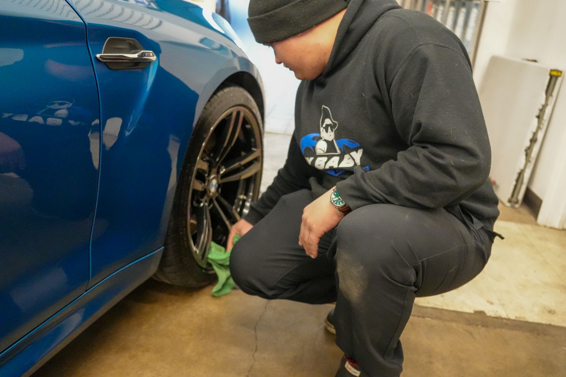A man is kneeling down next to a blue car in a garage.