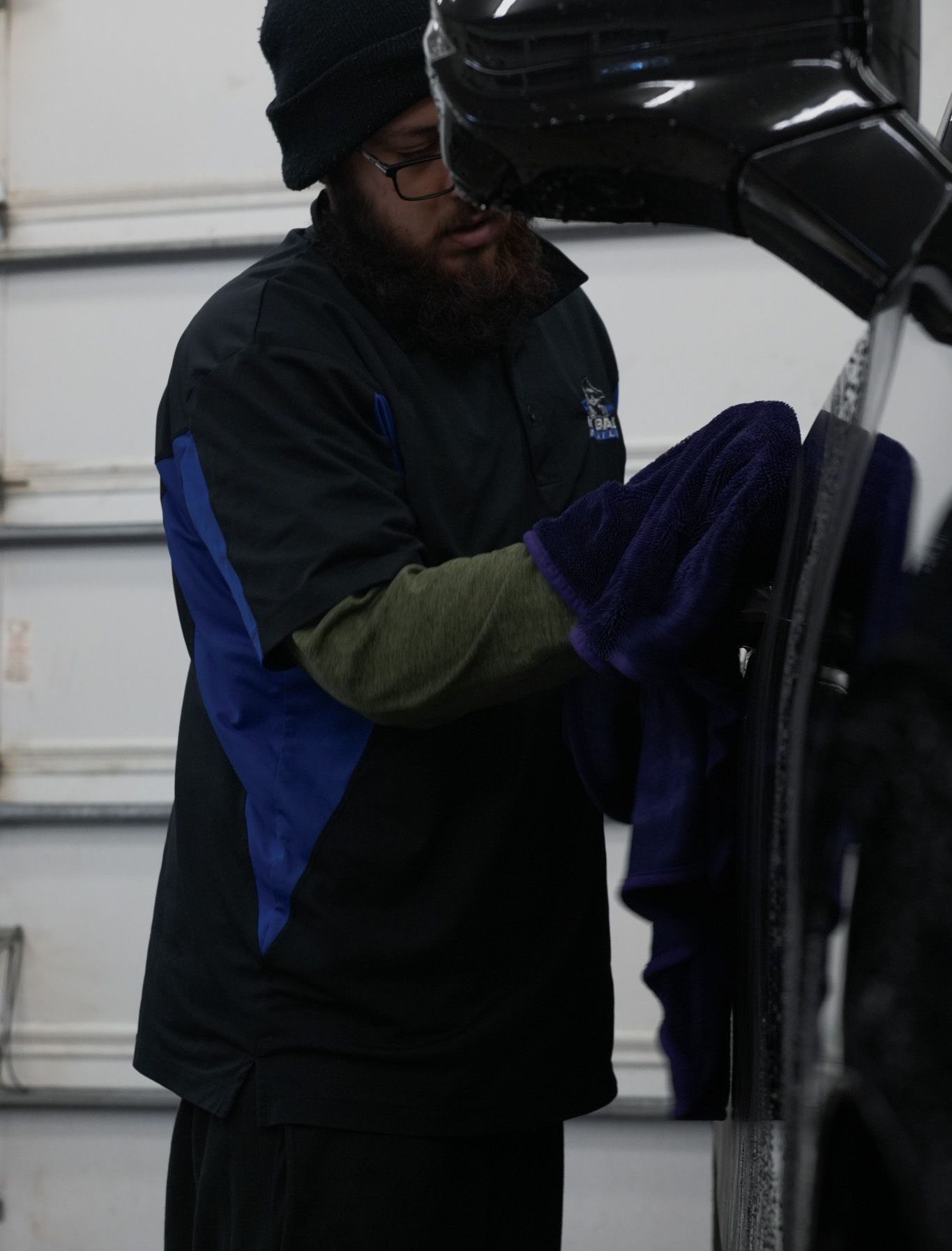 A man with a beard is cleaning a car with a towel