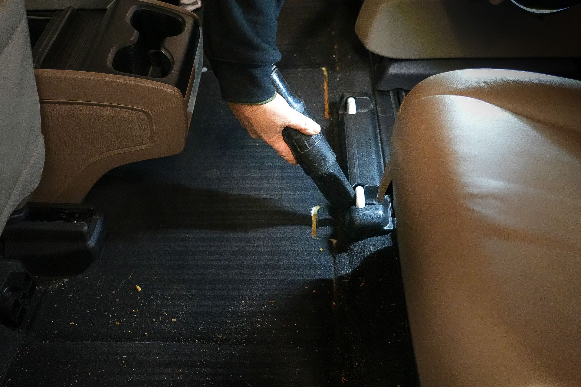 A person is using a vacuum cleaner to clean the floor of a car.