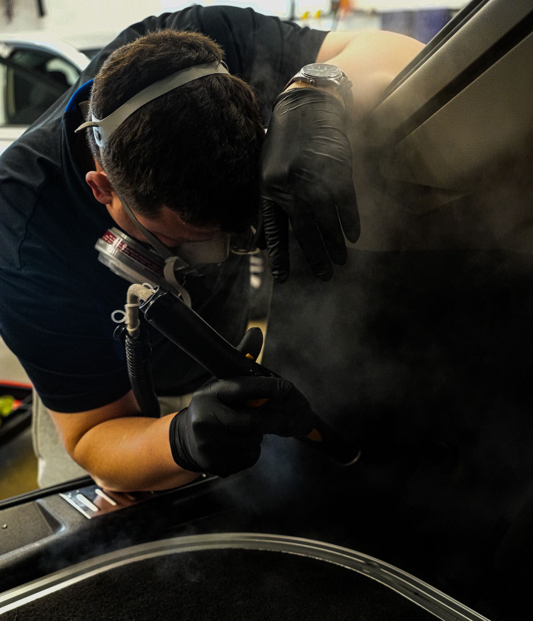 A man in a protective suit is cleaning the interior of a car.