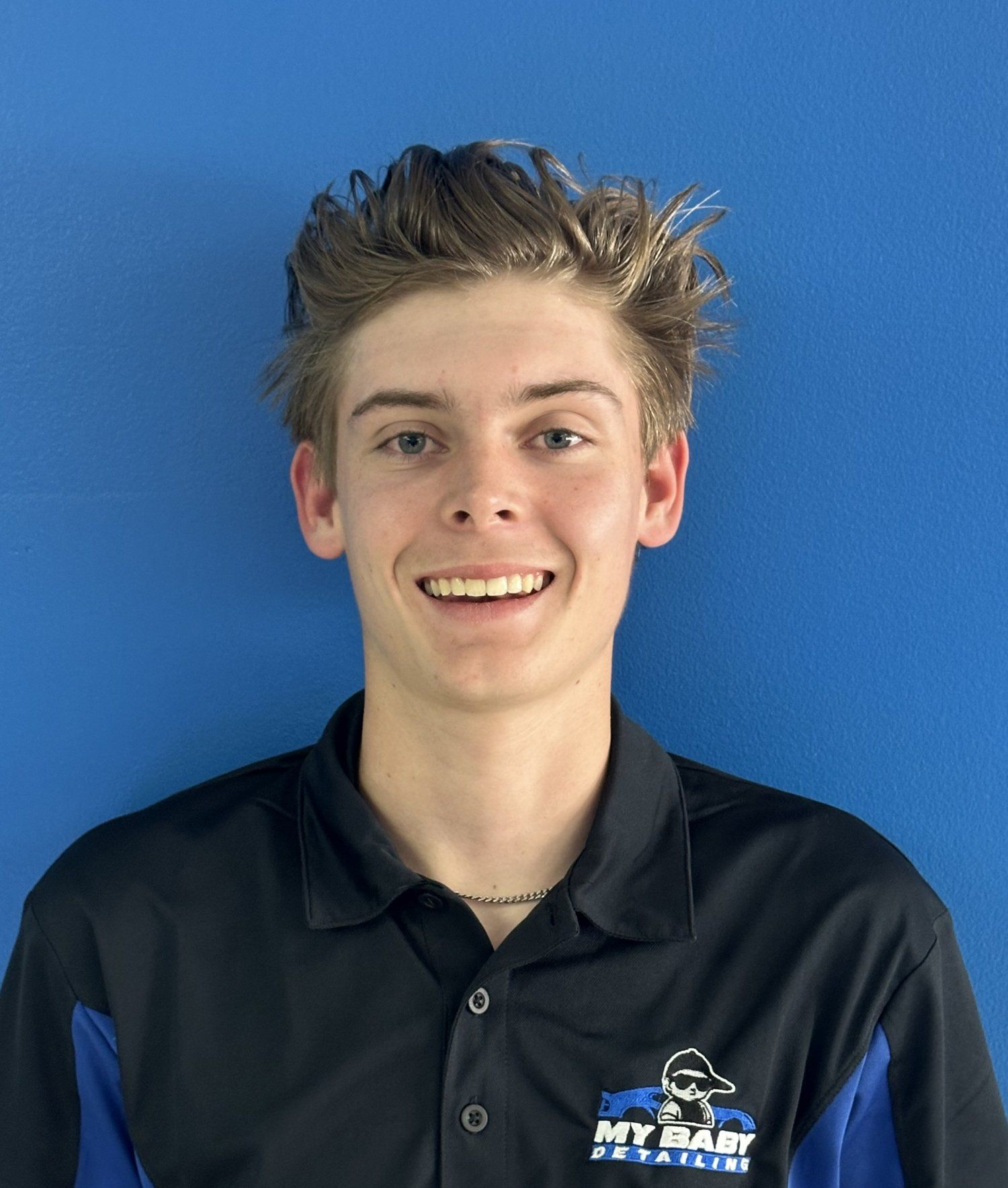 Young man smiling, wearing a black and blue polo shirt against a blue background.