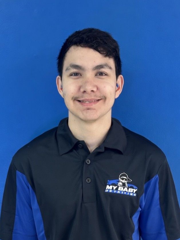 A person smiling against a bright blue background, wearing a black and blue collared shirt with a logo on the chest.