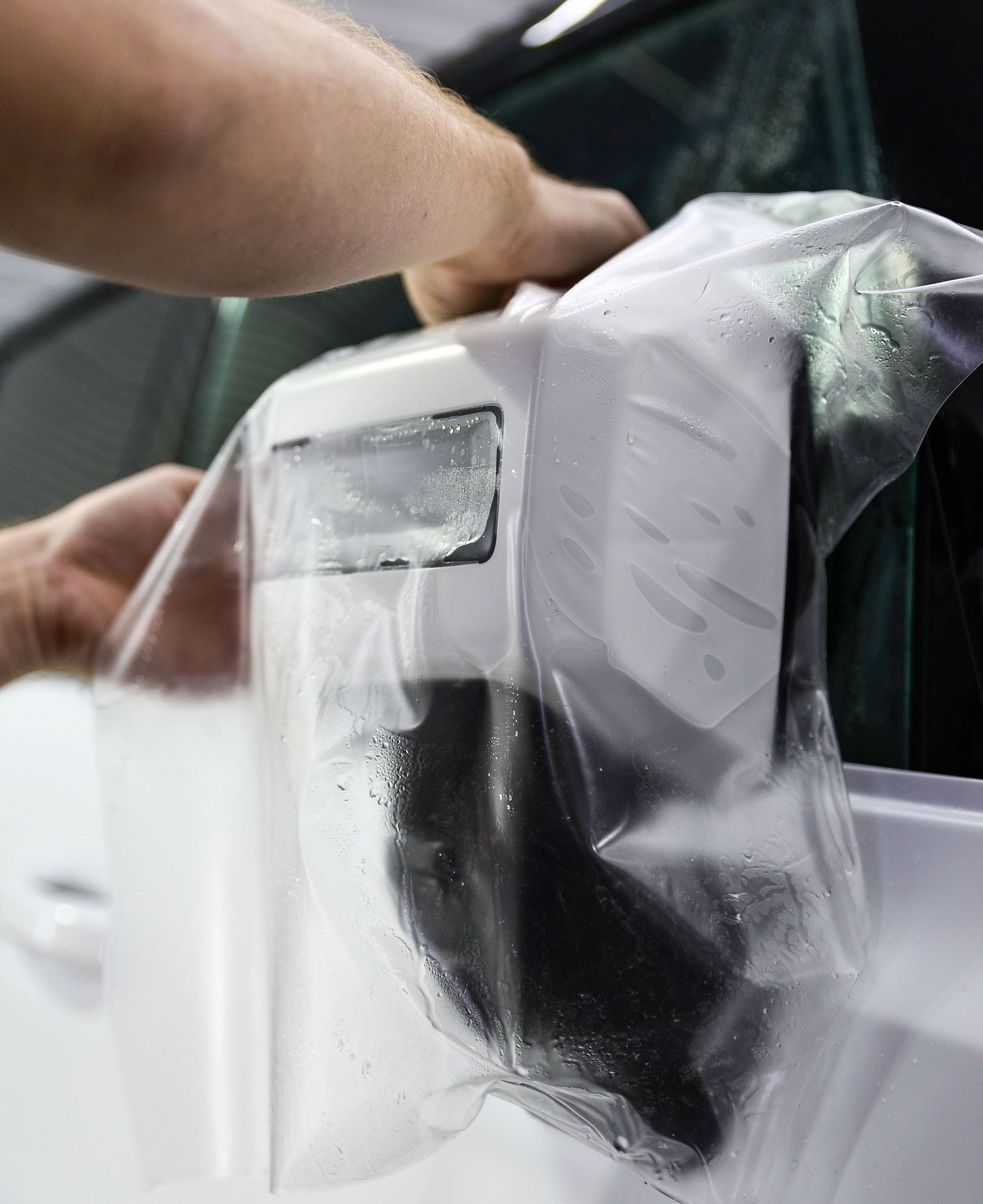 A person is wrapping a car with plastic wrap.