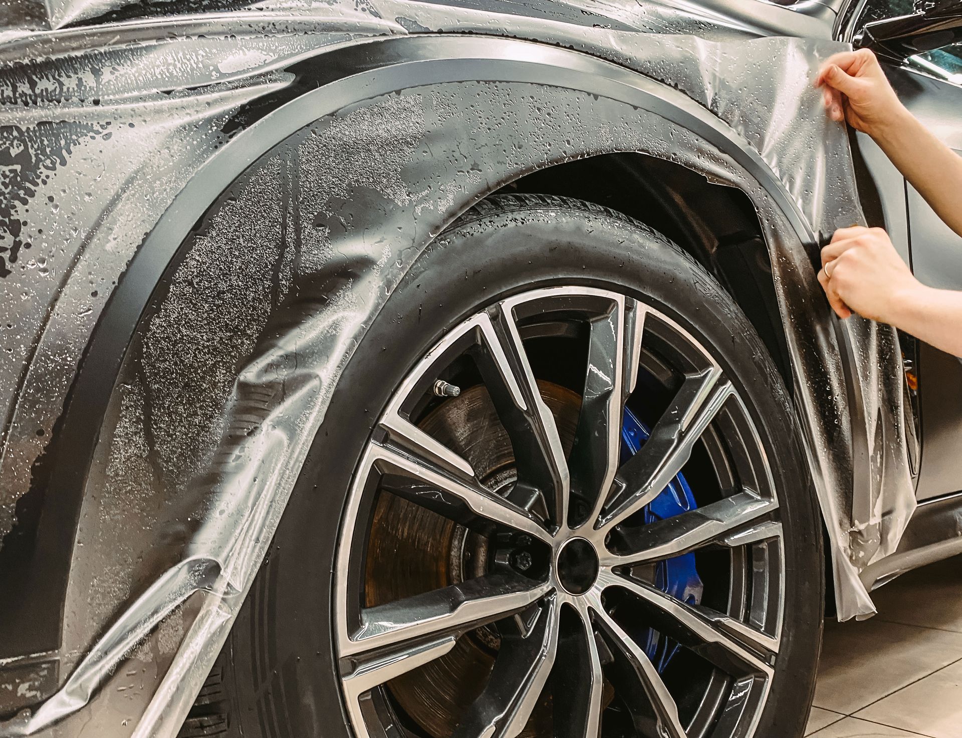 A person is applying a protective film to the fender of a car.