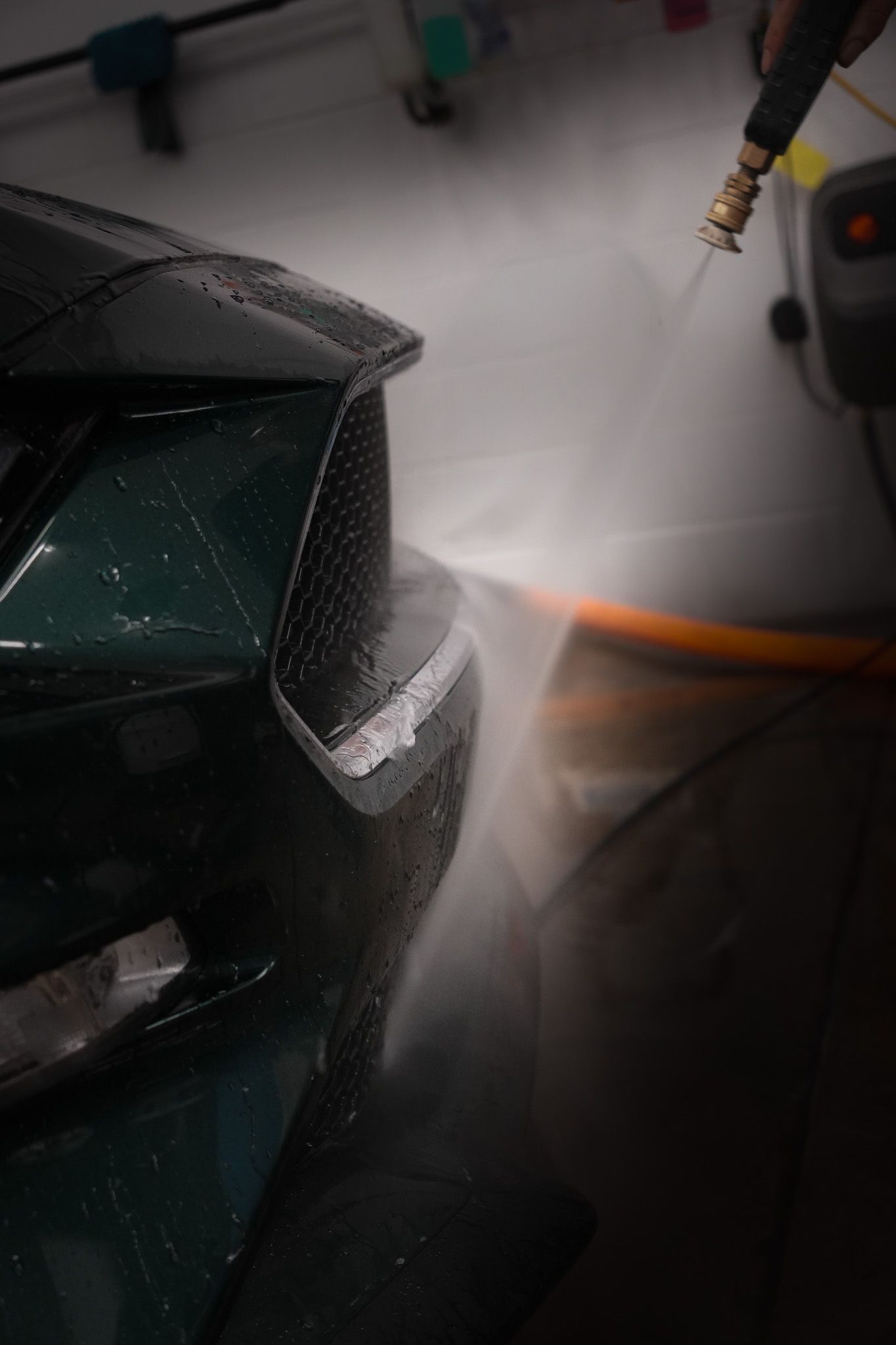 A person is washing a car with a hose in a garage.