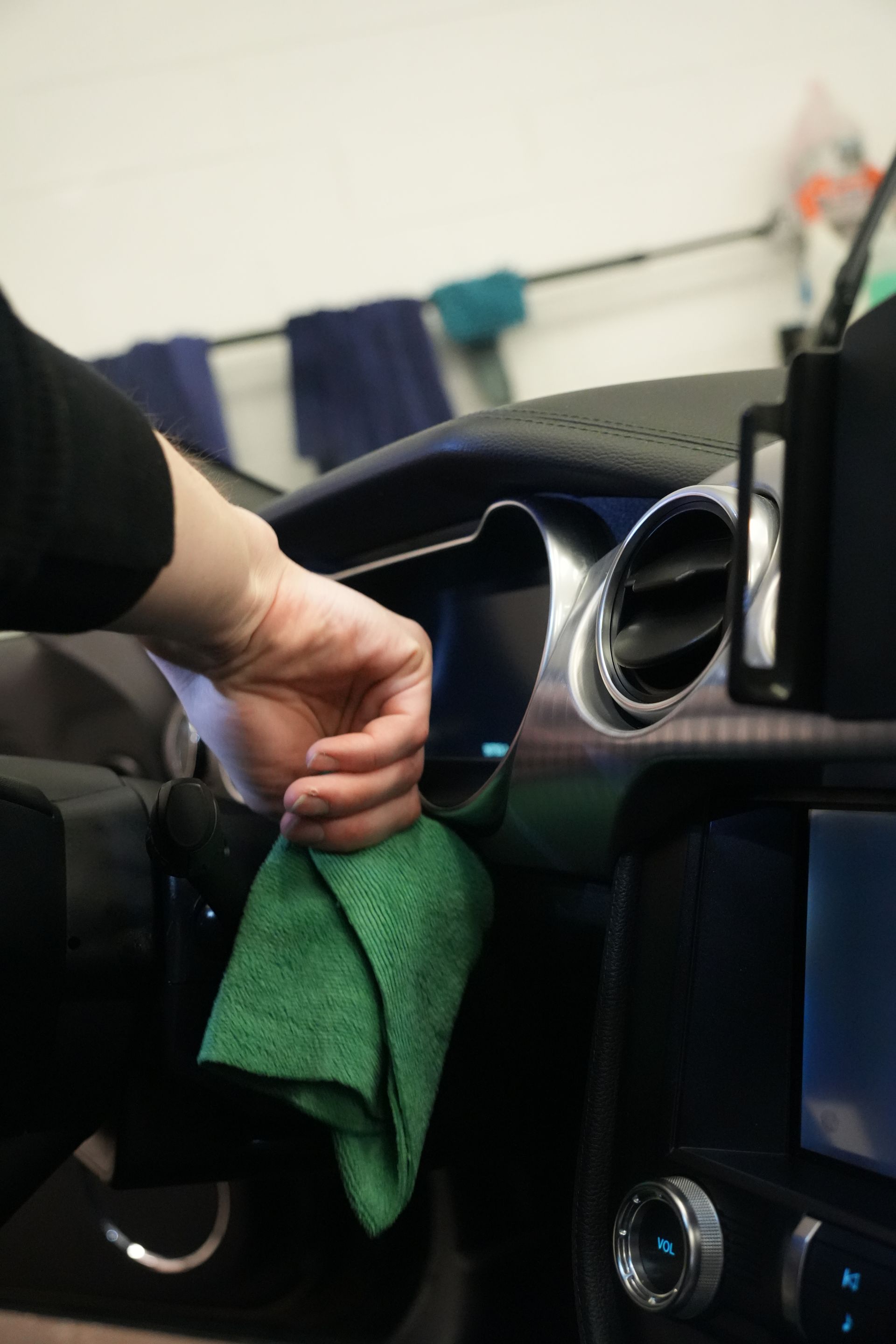 A person is cleaning the dashboard of a car with a green cloth.
