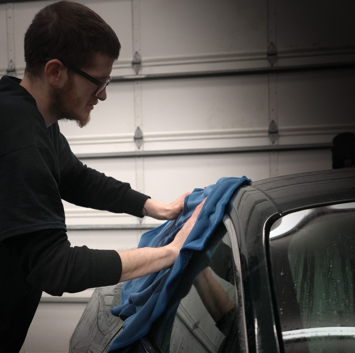 A person is applying ceramic coating to a black car.