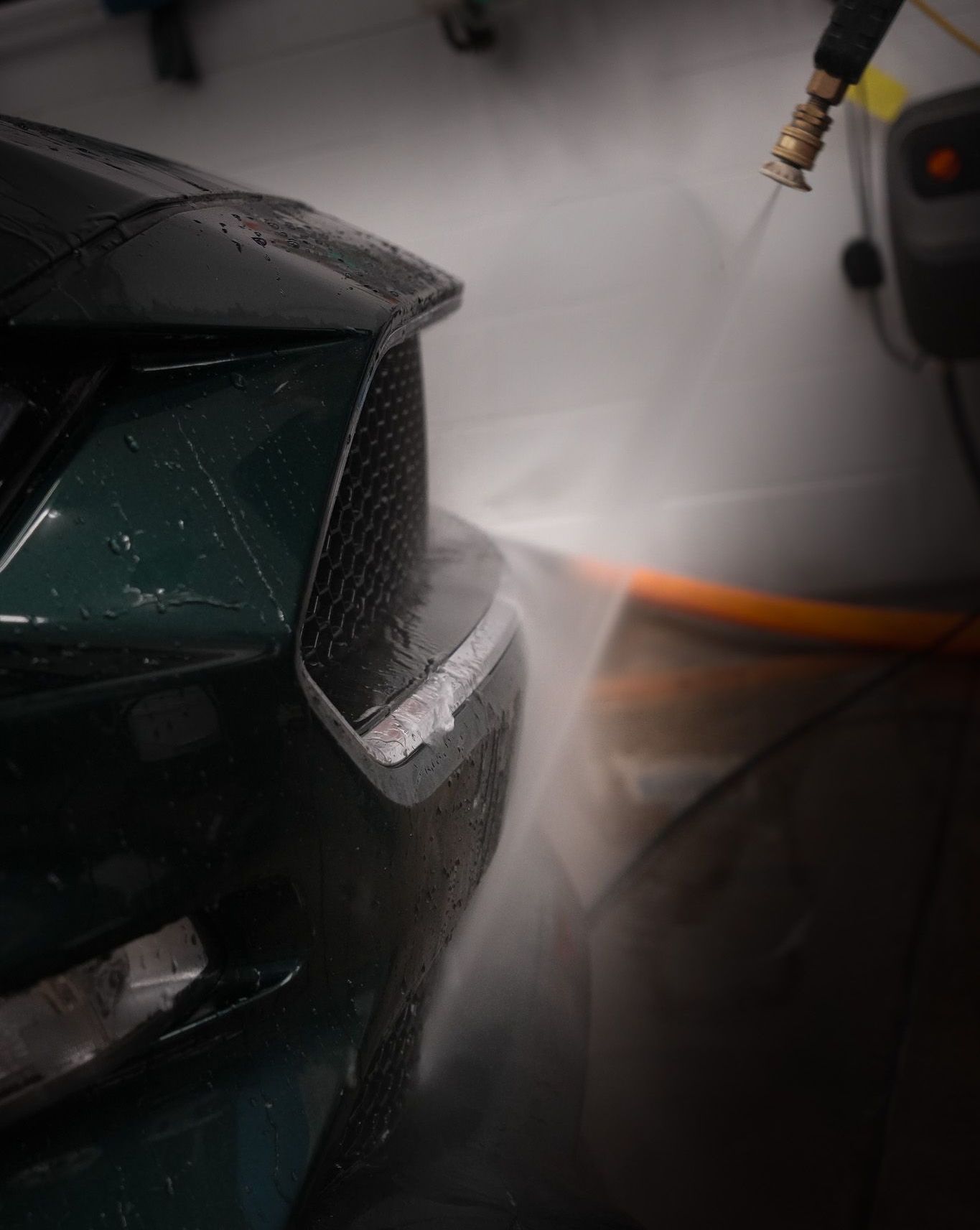 A close up of a car being washed with a high pressure washer.