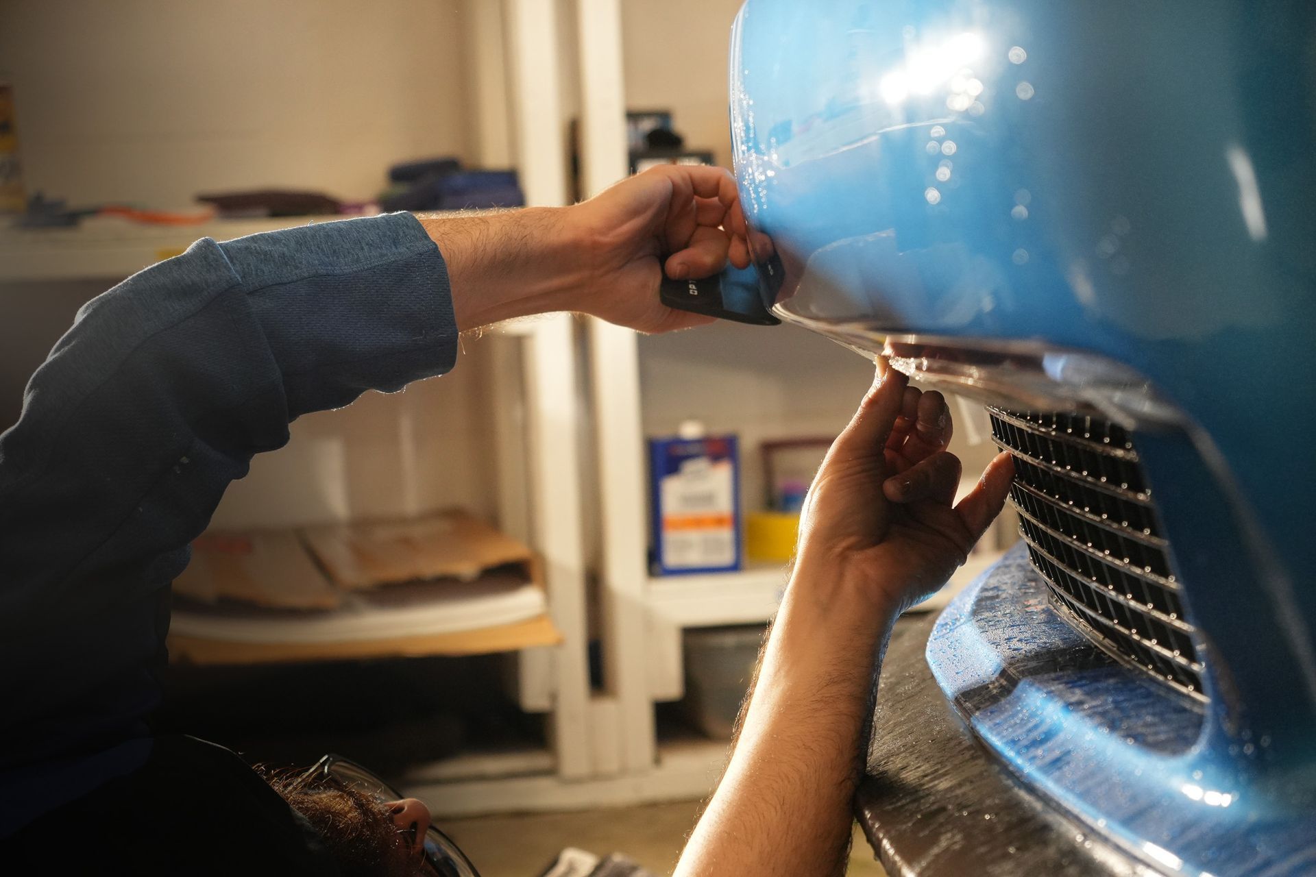 A man is working on a blue car in a garage.